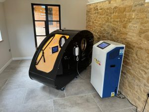 Black Winslet hyperbaric chamber with a transparent entrance door beside a white and blue control unit.